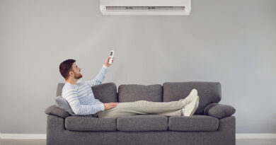 Jak dobrać moc klimatyzacji do pomieszczenia? Mężczyzna siedzący na kanapie pod klimatyzatorem ściennym.